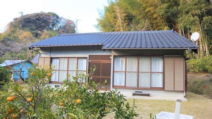 山あいにたたずむ平家のお試し滞在住宅「西川」と庭に植えられたミカンの木の画像