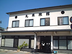 一階にガラス張りの玄関があり、二階には窓が四つある丸米旅館の外観画像。