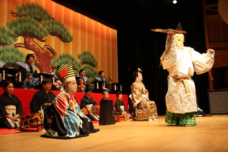 楽器を演奏する人とお面を付けた人が扇子を持ち土佐絵金歌舞伎を上演している写真