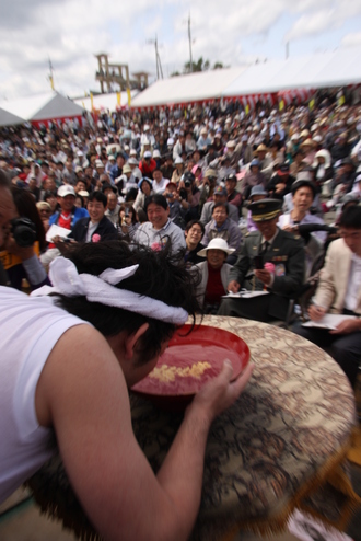 大杯になみなみとそそがれた「おらんくの酒」を一気に飲み干す男性と沢山の観客たちの写真