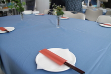 青いテーブルクロスの上に、空の白いお皿と赤い箸袋がセットでいくつか置かれている写真