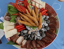 色鮮やか大皿に魚のフライや貝、豚肉の燻製、伊勢海老等が盛られている写真