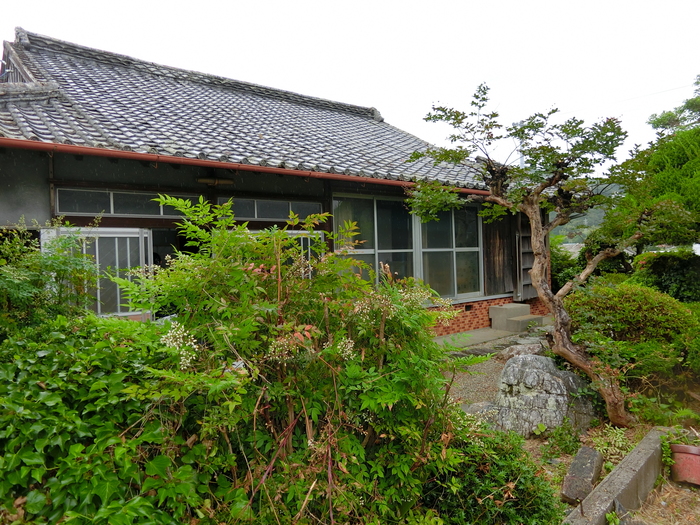 家の前に植物がお生い茂っている空き家（瓦屋根の平屋）の全体の写真