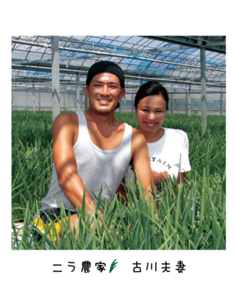 青空の下、畑に座り笑顔のニラ農家古川さん夫妻を正面から写した写真
